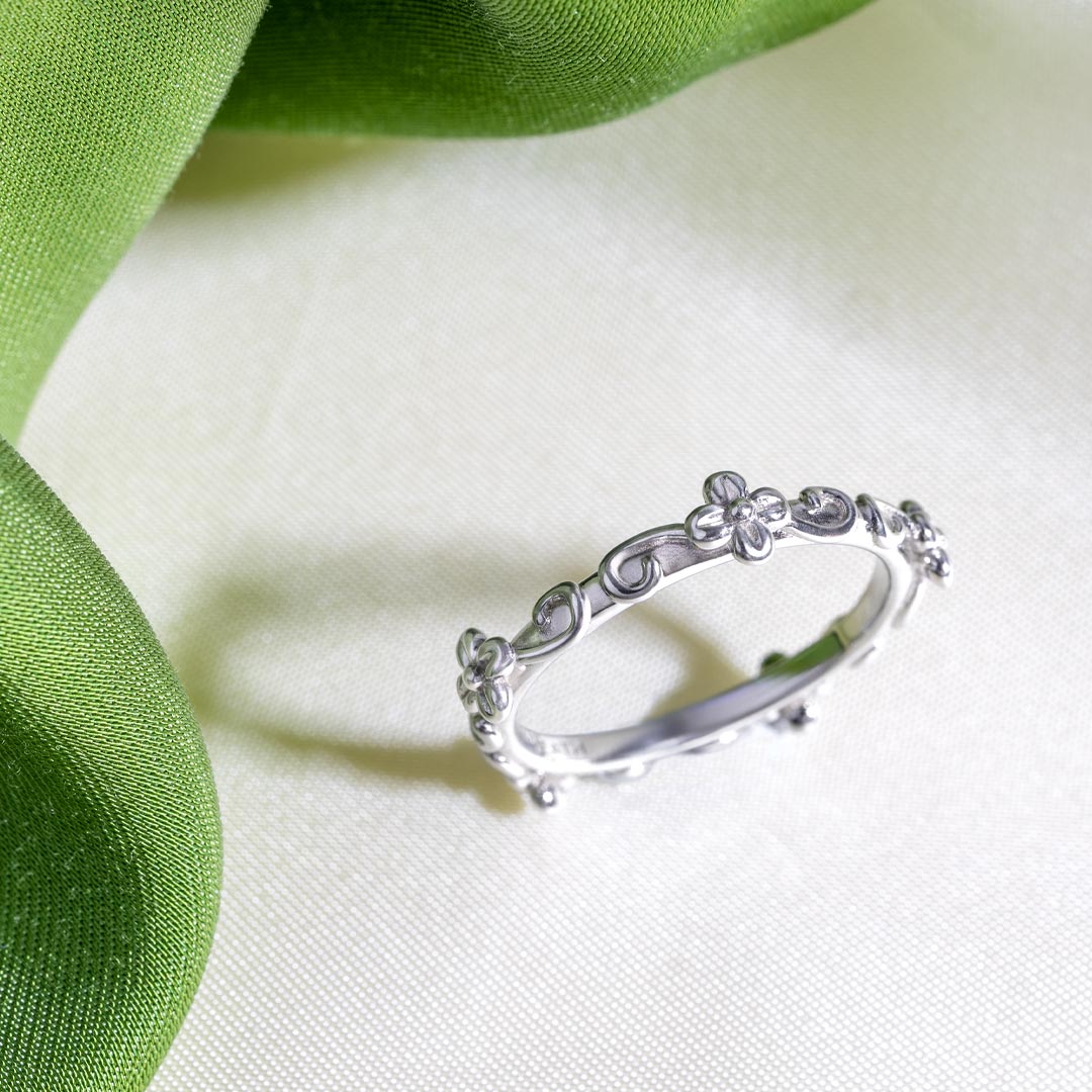 Silver ring with floral design on a green fabric background