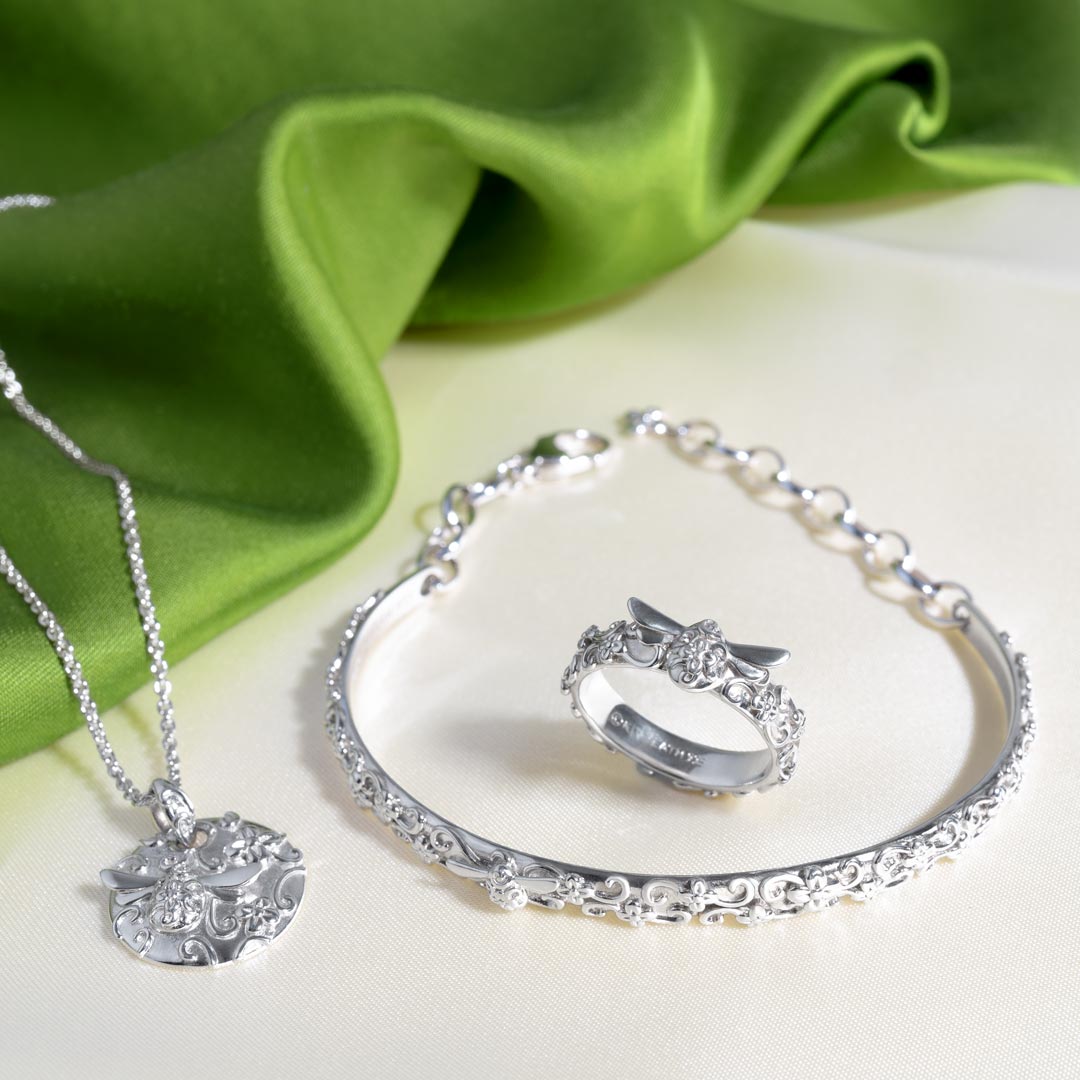 Silver jewelry set including a necklace, bracelet, and ring on a green fabric background