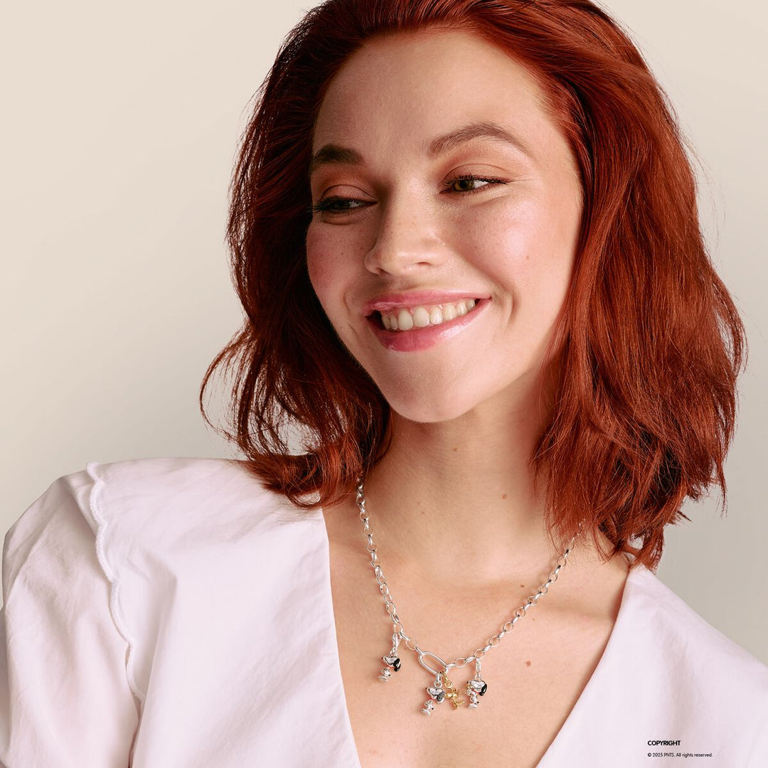Woman with red hair wearing a necklace on a plain background