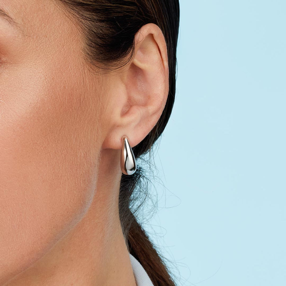Silver hoop earring worn by a person with a light blue background