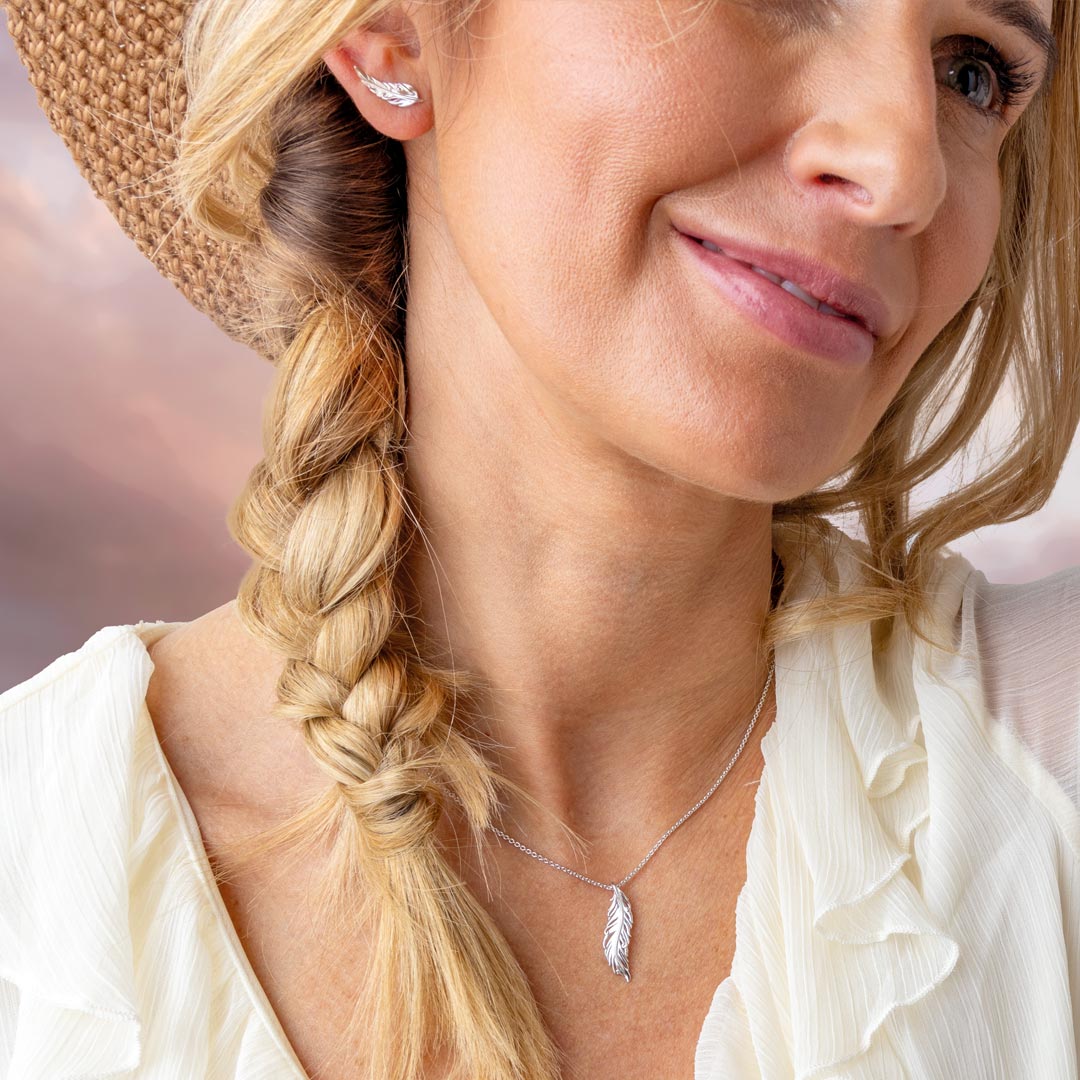 Woman with braided hair wearing a straw hat and a necklace with a feather pendant.