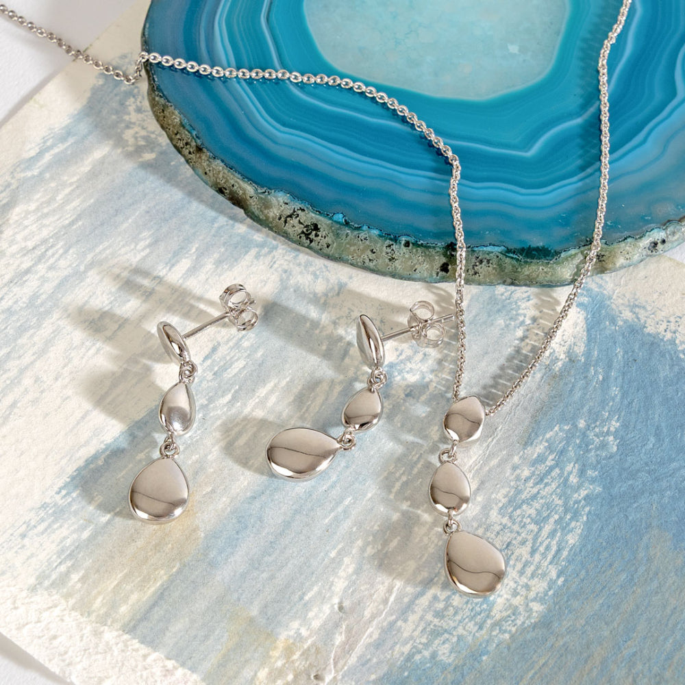 Silver jewelry set with necklace and earrings on a textured surface