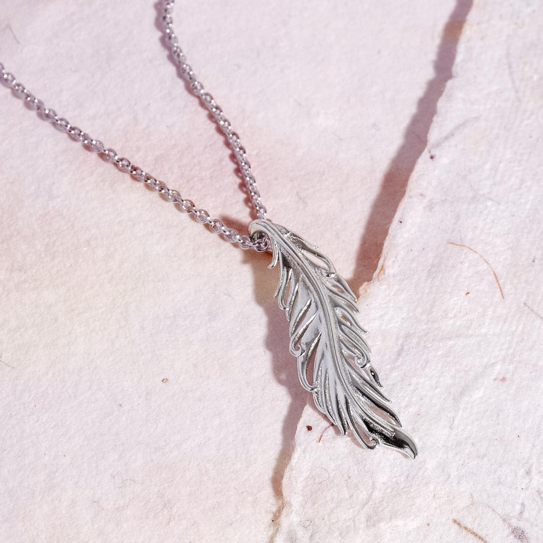Silver feather necklace on a textured white surface