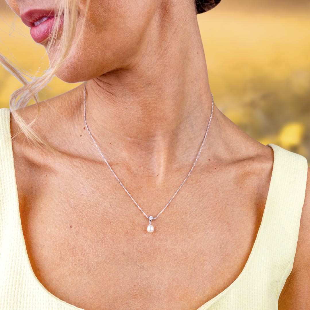 Woman wearing a delicate necklace with a pearl pendant against a blurred natural background