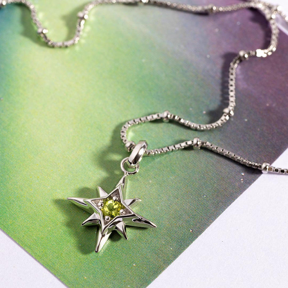 Silver necklace with a star-shaped pendant featuring a green gemstone on a white background.