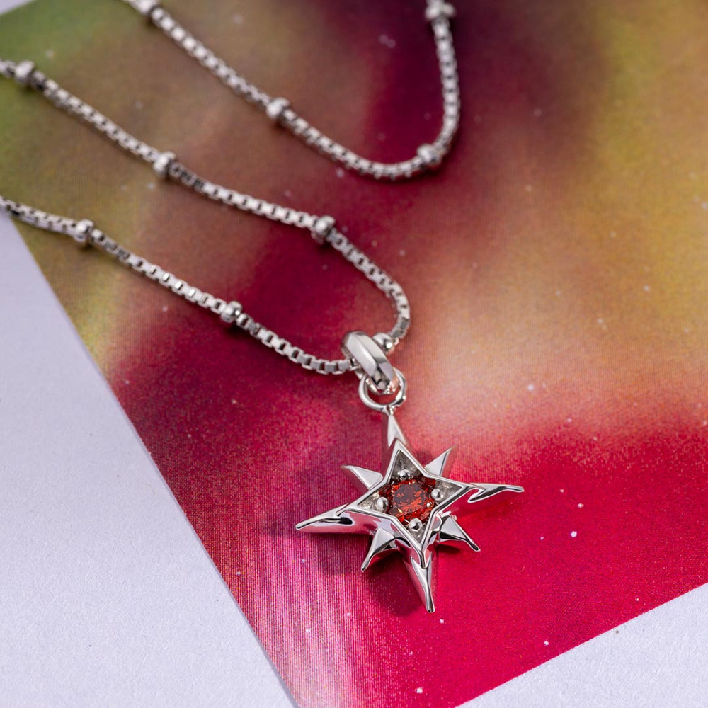 Silver star-shaped pendant with a red gemstone on a chain against a colorful background