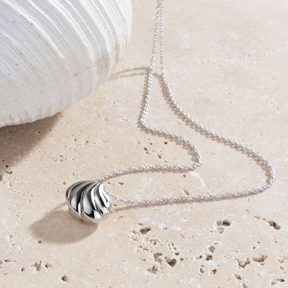 Silver necklace with a shell pendant on a sandy surface