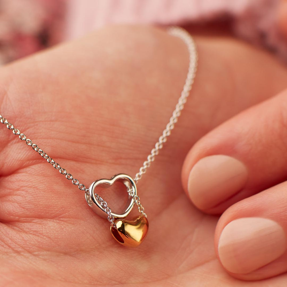 Gold heart-shaped pendant on a silver chain held in a hand.