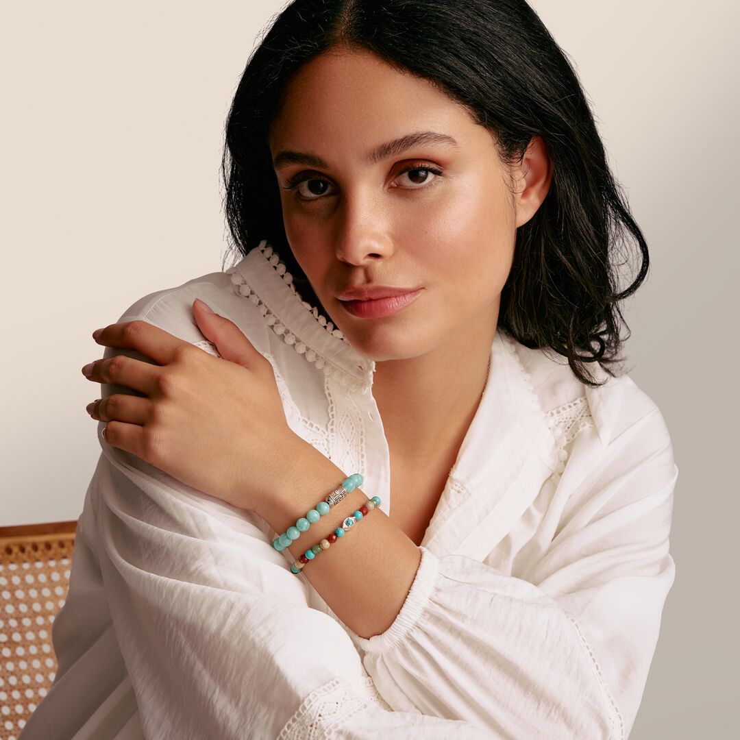 Woman wearing a white outfit with a textured collar, holding her arm over her chest, against a neutral background.