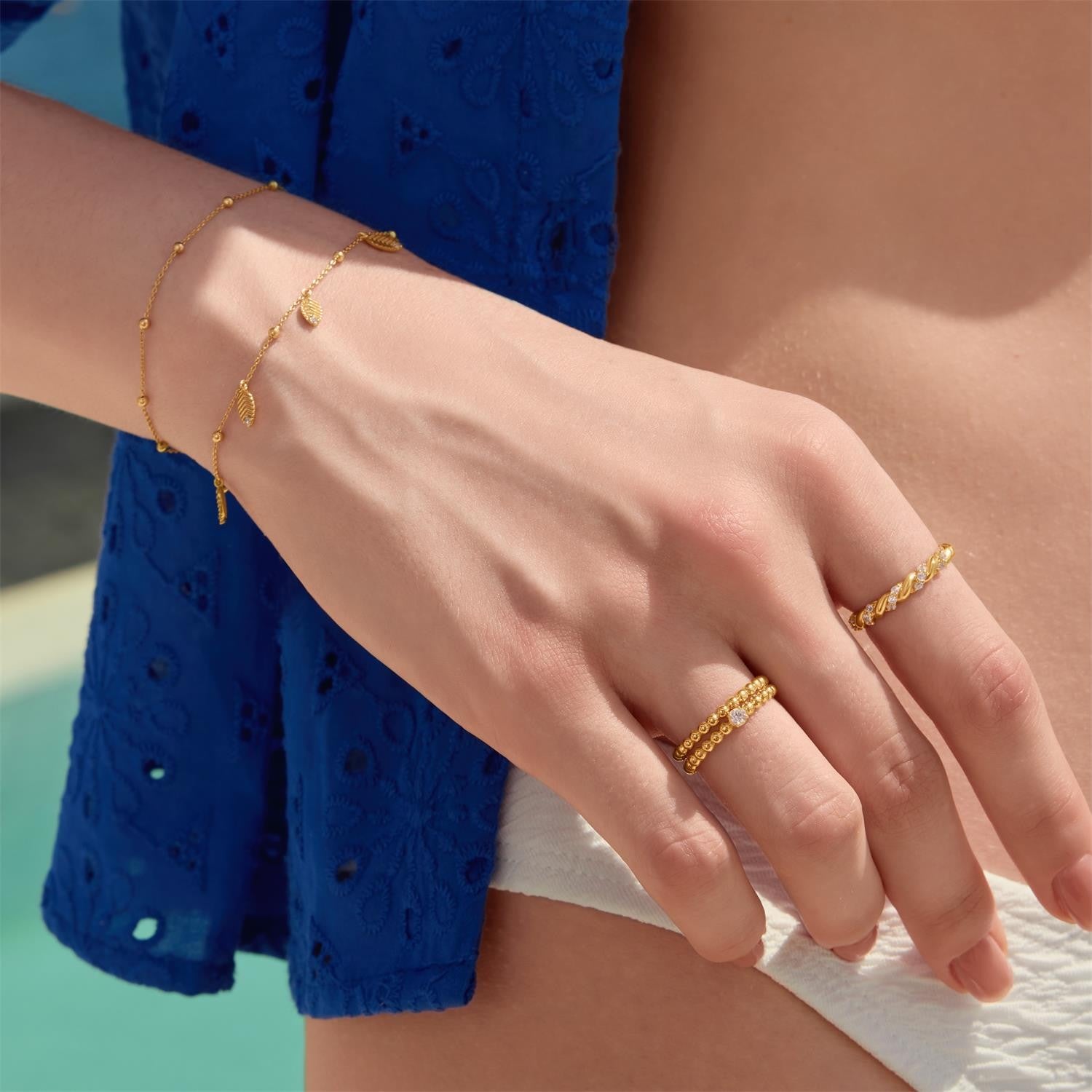 Gold bracelets and rings on a person's wrist and hand against a blue dress background