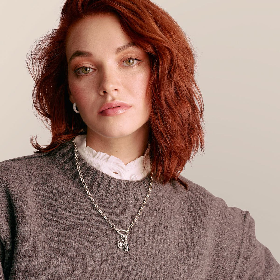 Woman wearing a gray sweater and silver necklace with a pendant on a neutral background