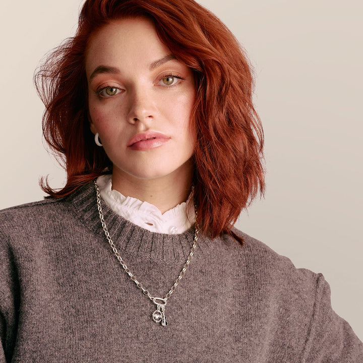 Woman wearing a gray sweater and silver necklace with a pendant on a neutral background