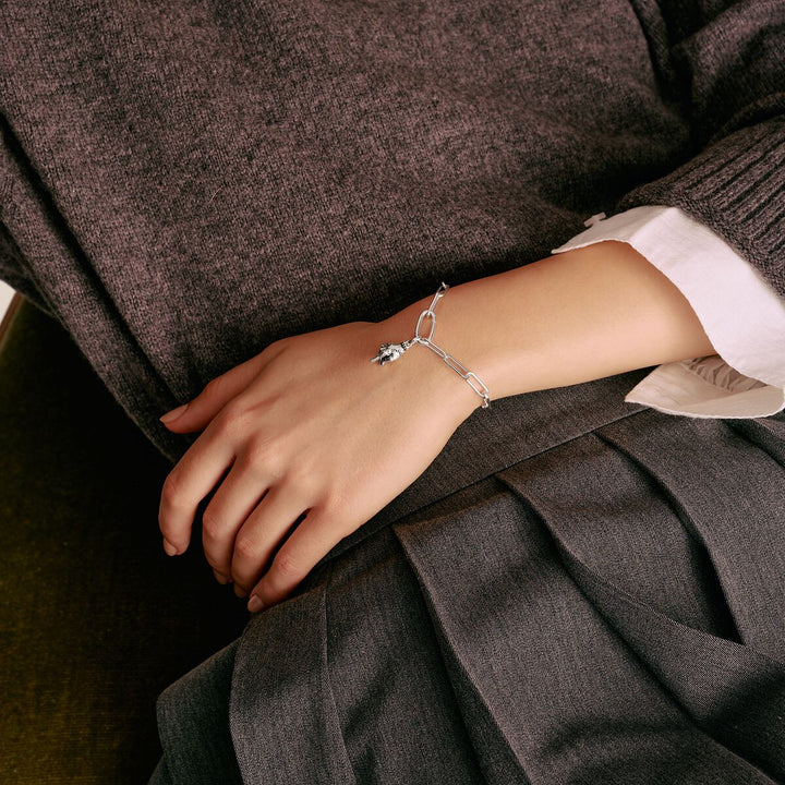 Person wearing a silver bracelet with a dark setting on a brown textured fabric background
