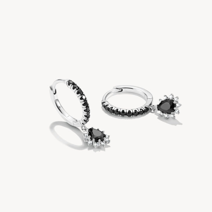 Pair of silver hoop earrings with black gemstones on a white background