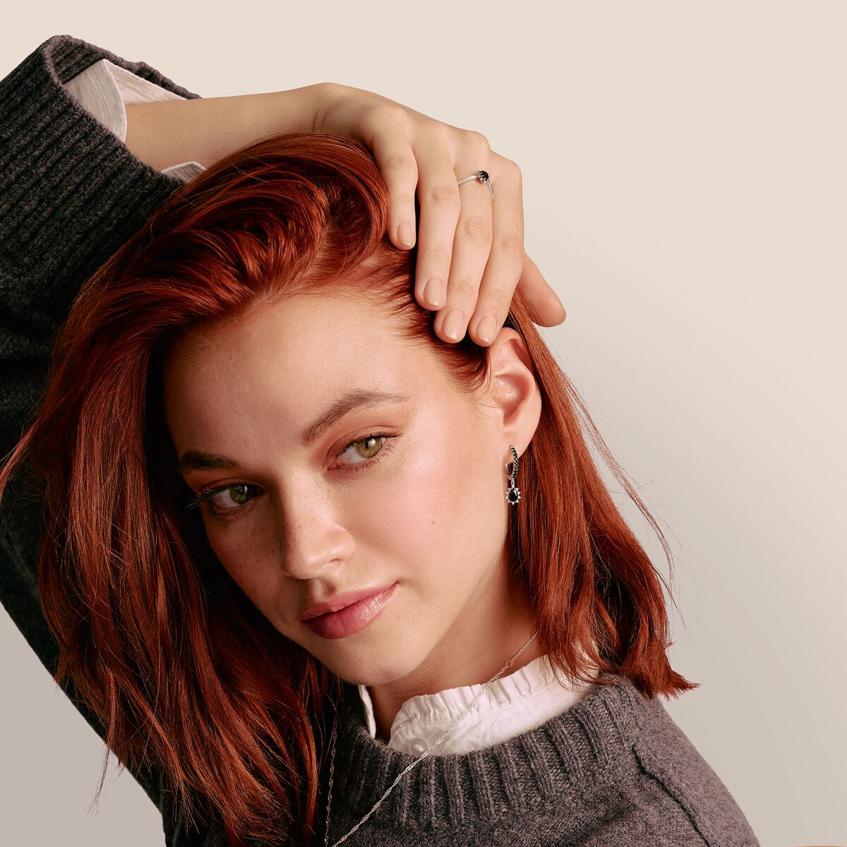 Woman with red hair being touched by a hand against a neutral background