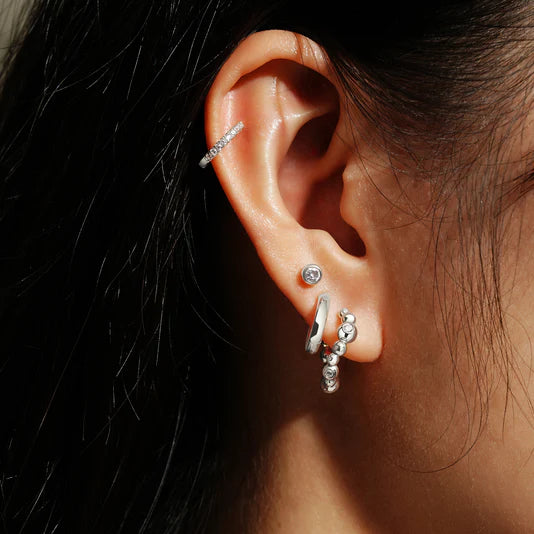 Close-up of an ear with multiple silver earrings against a dark background