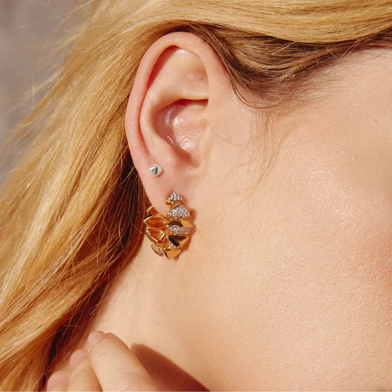 Close-up of a person wearing a gold earring with clear stones.