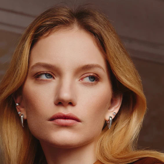 Close-up of a woman with blonde hair and earrings against a neutral background