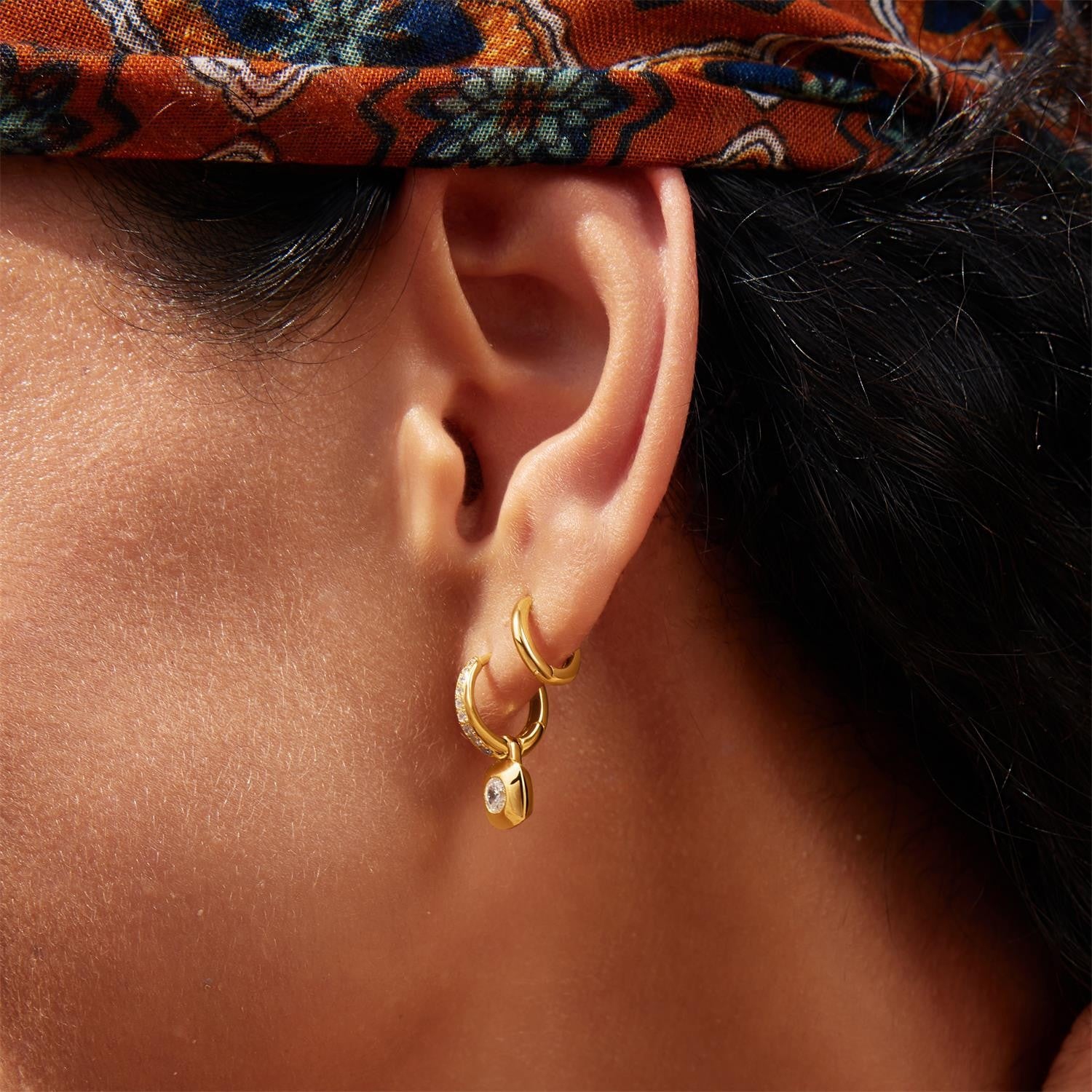Close-up of an ear wearing gold hoop earrings with a patterned headband.