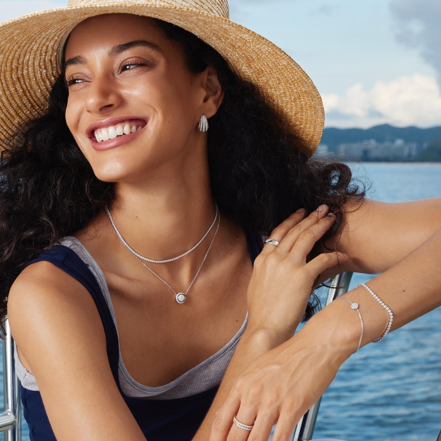 Woman wearing jewelry by a body of water with mountains in the background
