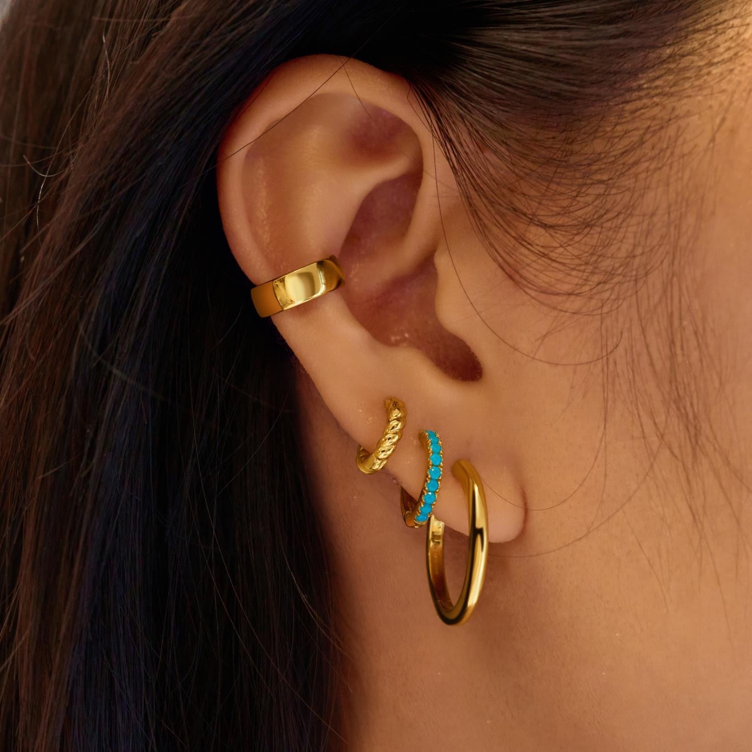 Close-up of an ear with gold hoop earrings and a turquoise stone.