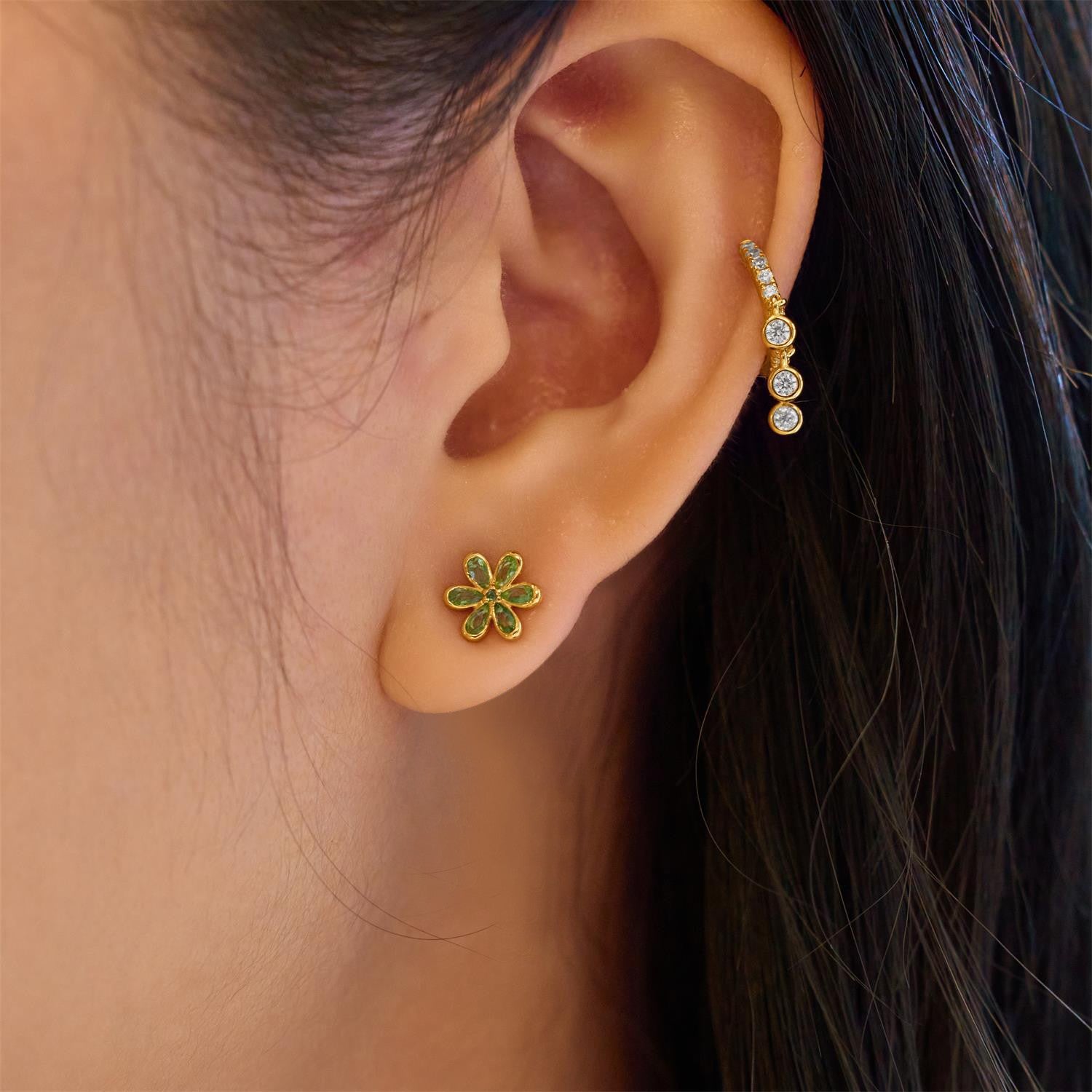 Close-up of an ear wearing a gold and green flower-shaped earring.