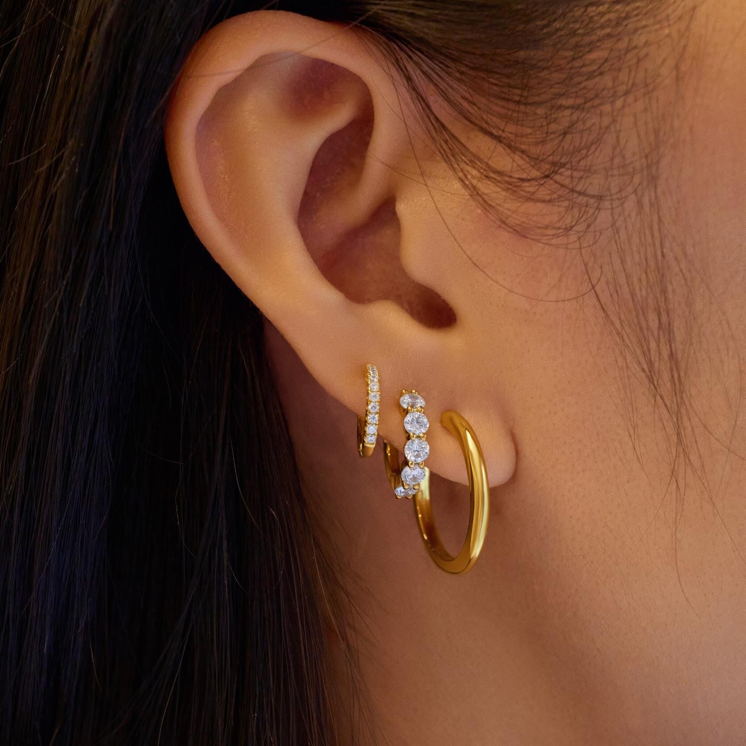 Close-up of an ear wearing gold hoop earrings with small diamonds.