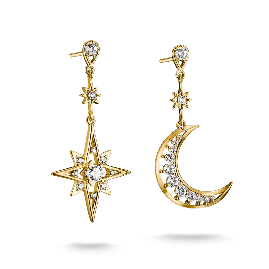 A pair of gold dangle earrings on a clean white background. One earring features a starburst motif with clear gemstones, and the other features a crescent moon with a row of clear gemstones along its curve.