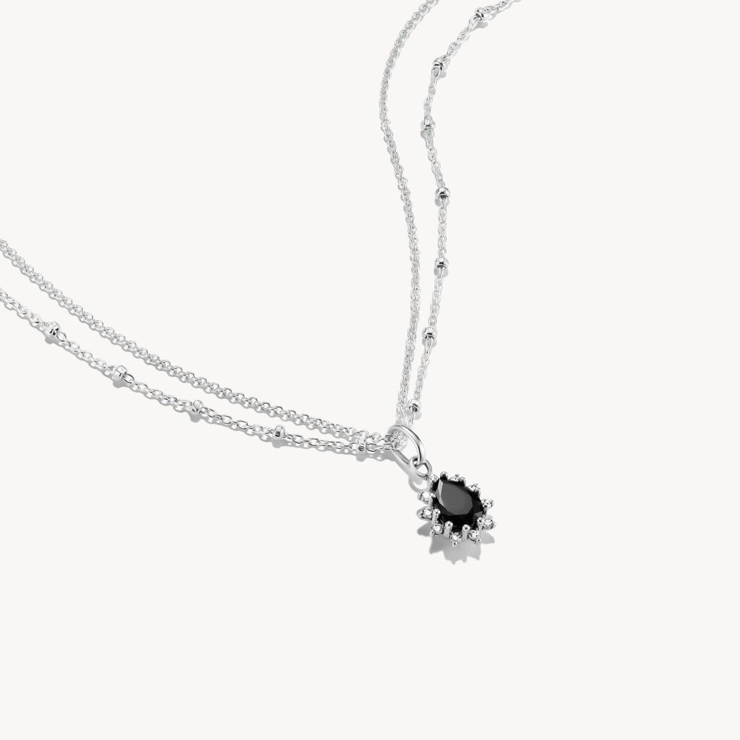 Silver necklace with a black gemstone pendant on a white background