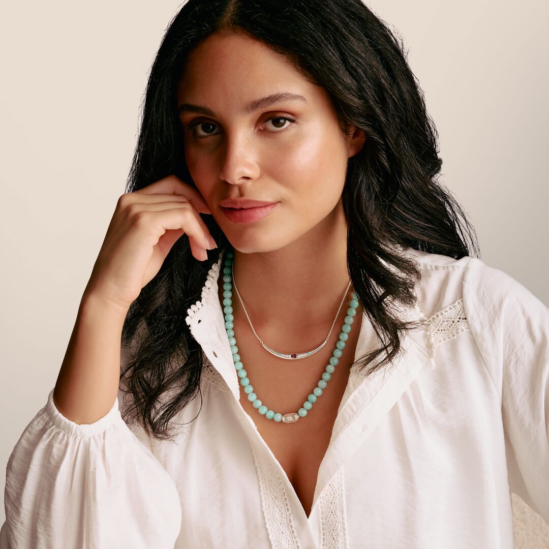 Woman wearing a white blouse and turquoise necklace against a beige background