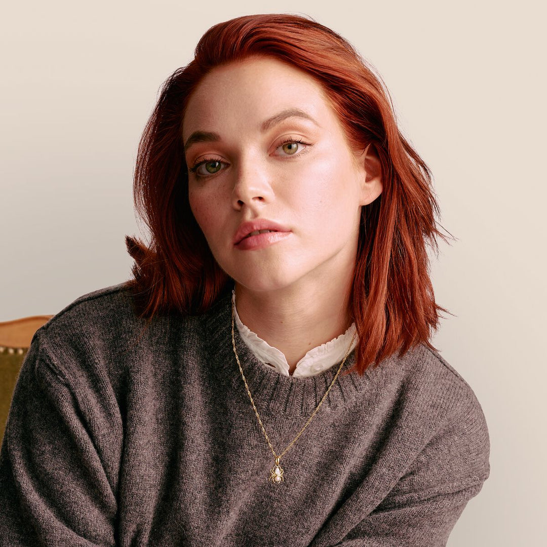 Woman with red hair wearing a gray sweater against a beige background