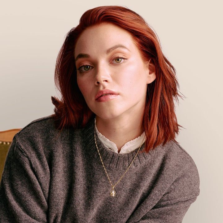 Woman with red hair wearing a gray sweater against a beige background
