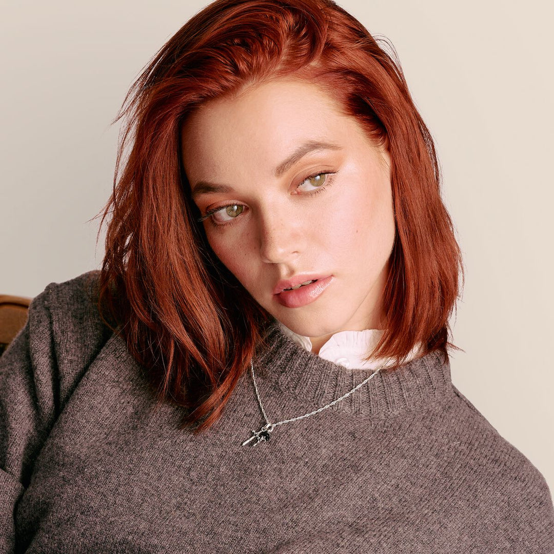 Woman with red hair wearing a gray sweater against a beige background