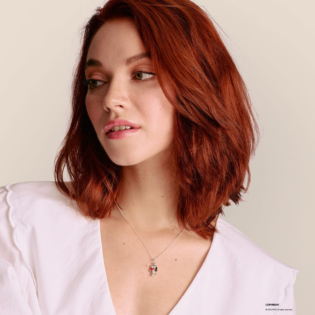 Woman with red hair wearing a white shirt and a necklace with a pendant on a light background