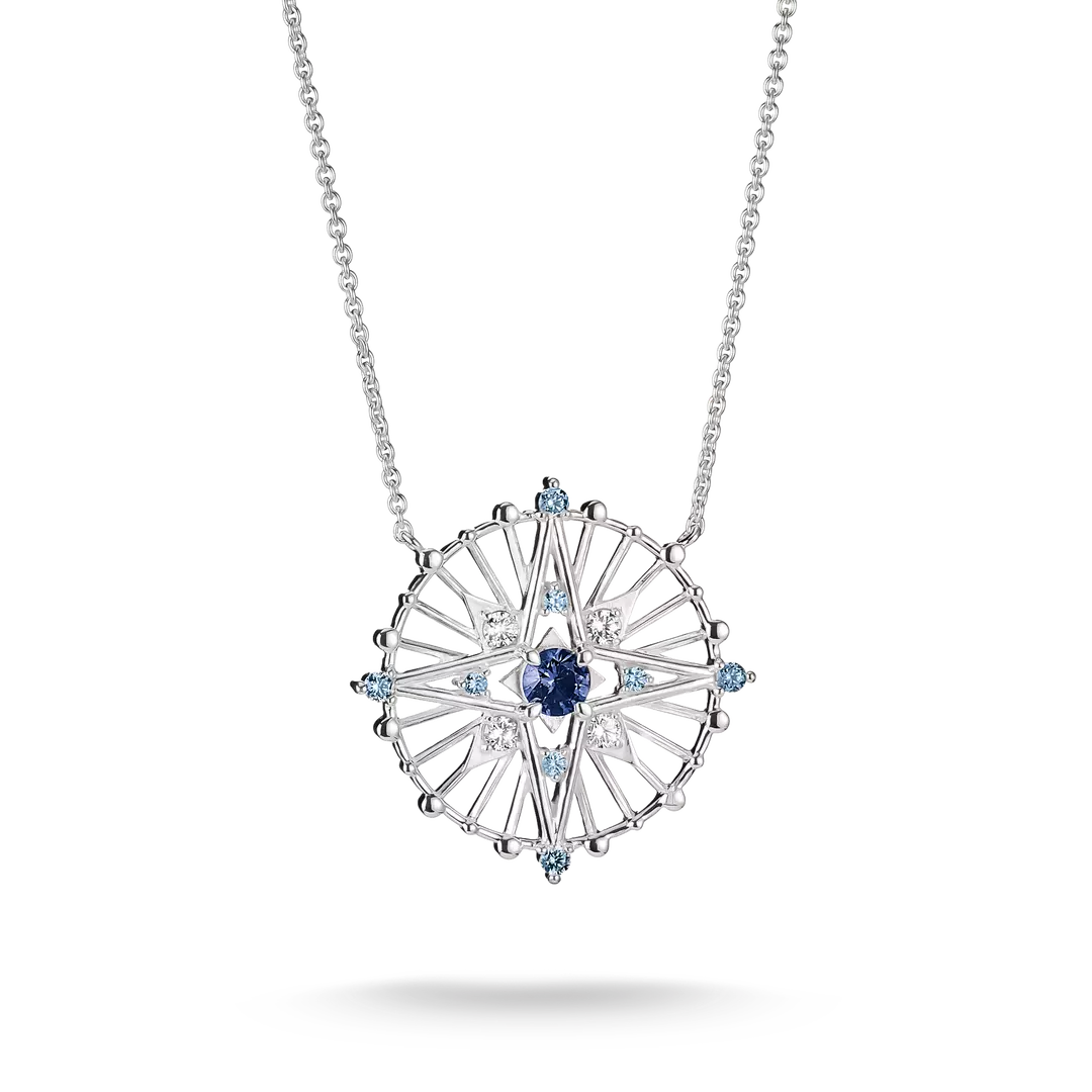 A silver-toned circular pendant necklace featuring a central deep blue sapphire surrounded by clear and light blue accent stones, suspended from a delicate silver chain on a white background.