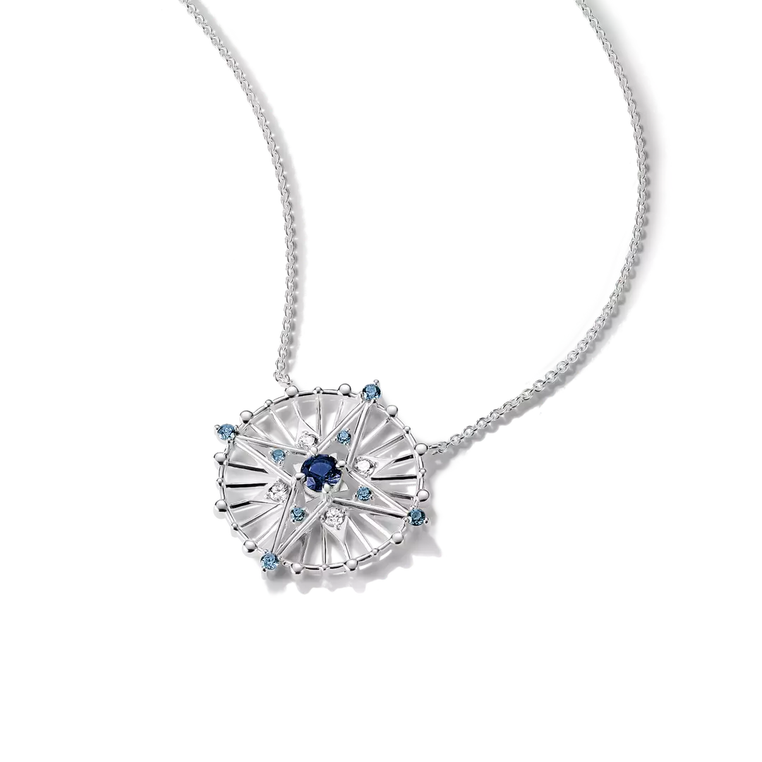 A silver-toned necklace featuring a circular sunburst pendant with a central dark blue gemstone and small light blue accent stones, shown on a clean white background.