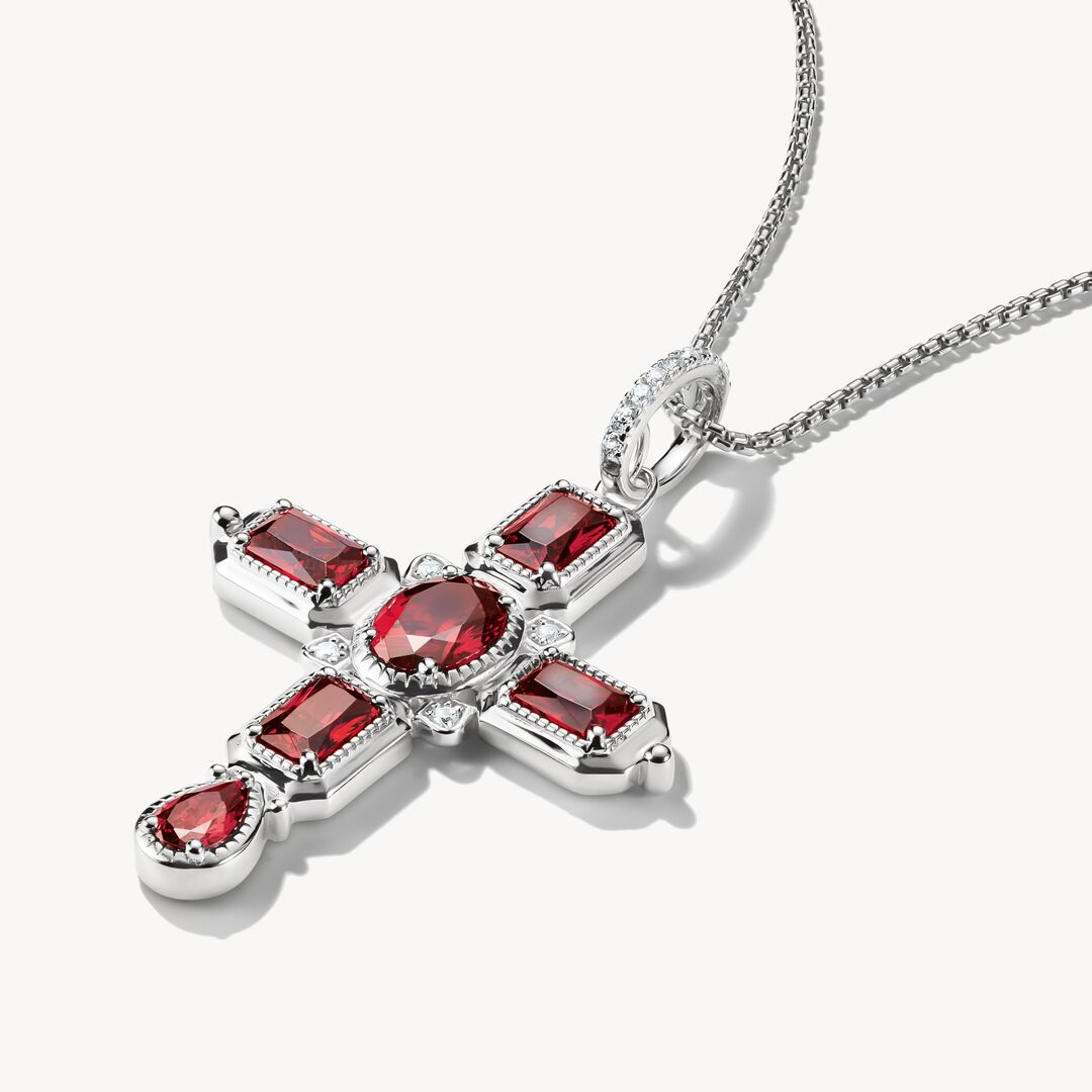 Silver cross pendant with red gemstones on a white background