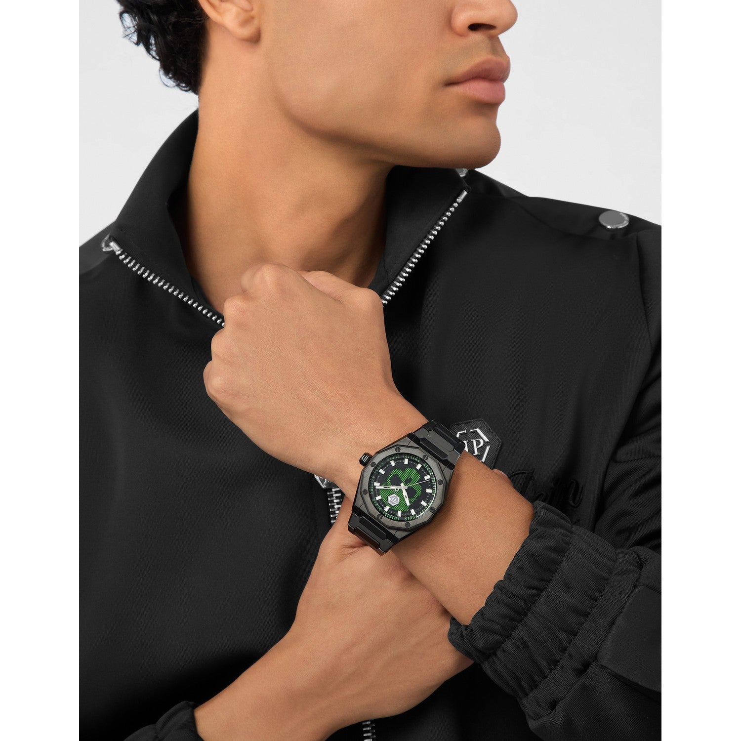 Person wearing a black watch with a green face on a plain background