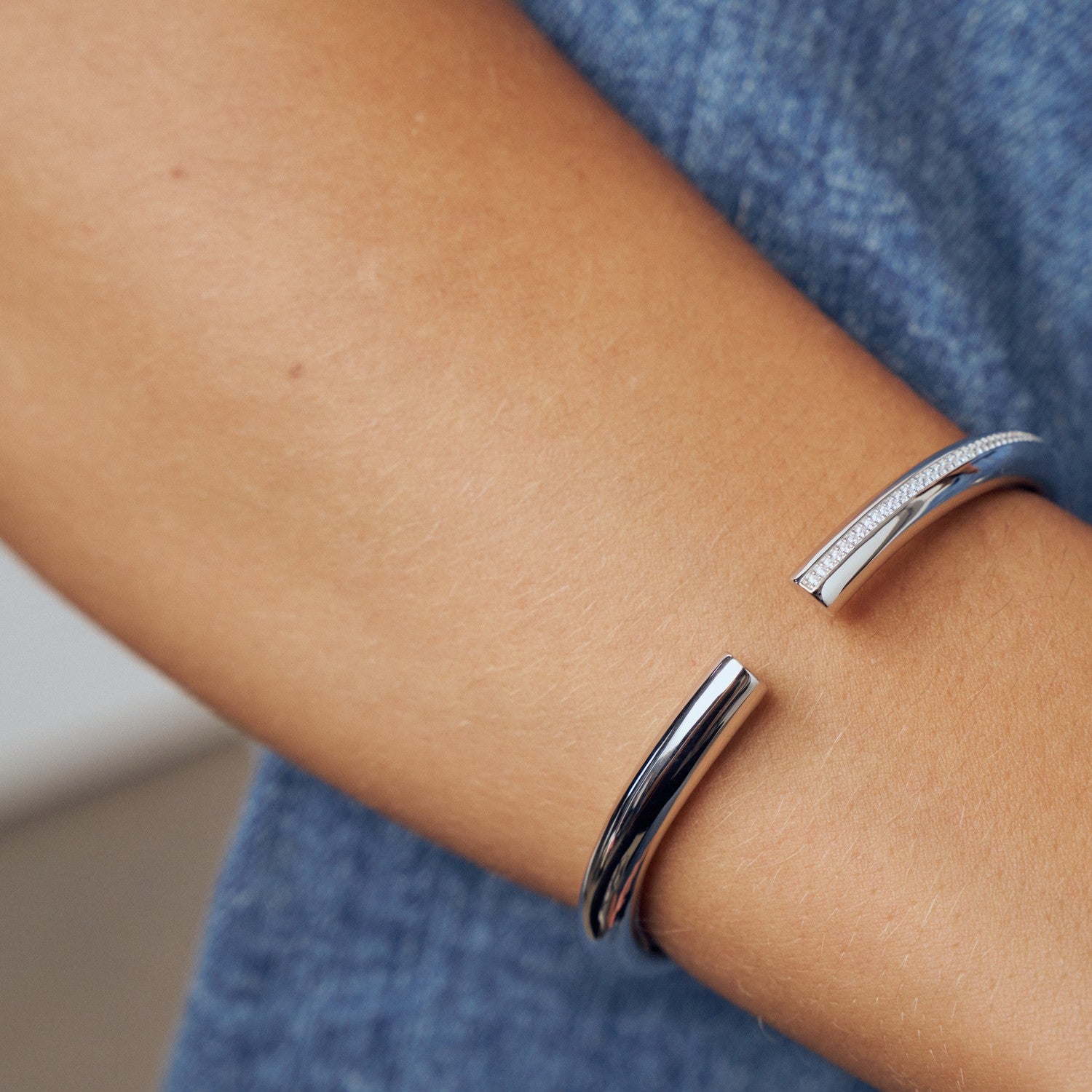 Silver bracelets on a person's wrist with a blurred blue background