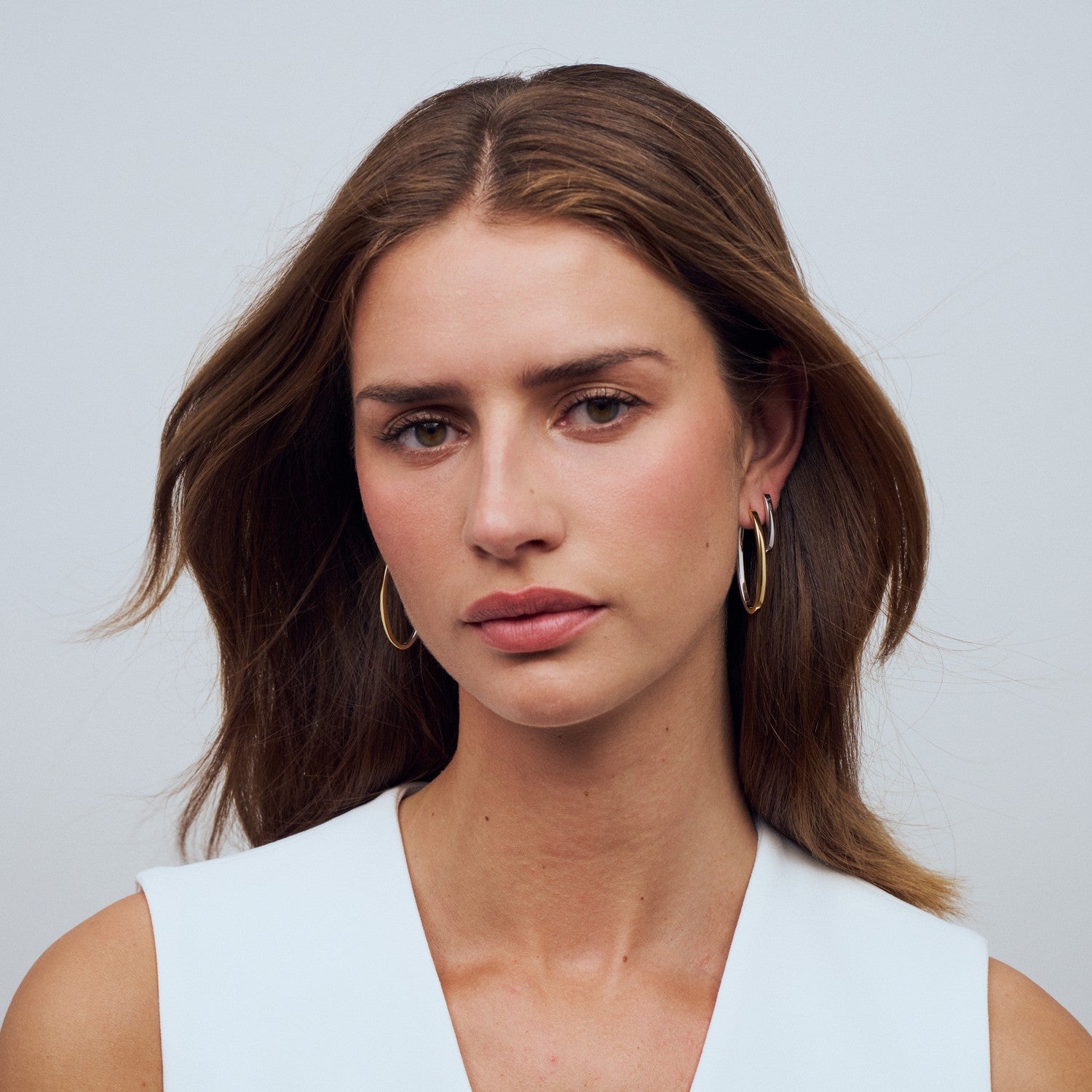 Woman with long brown hair wearing gold hoop earrings against a light gray background