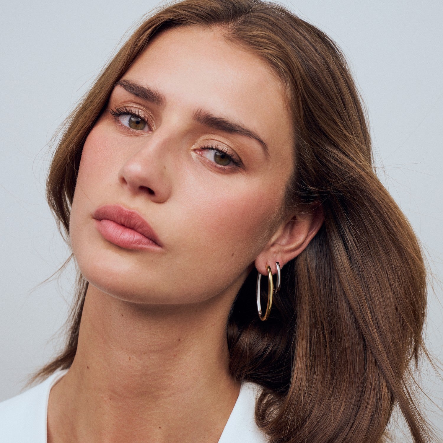 Woman wearing gold hoop earrings against a plain background