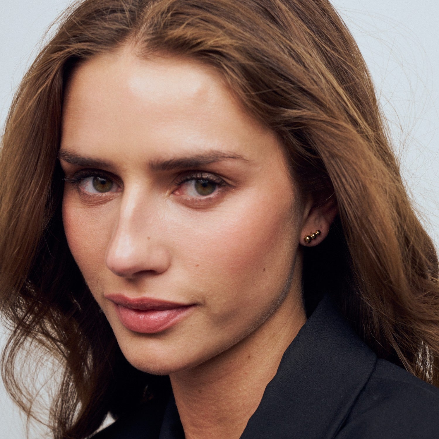 Close-up of a woman with long brown hair wearing a black blazer against a neutral background