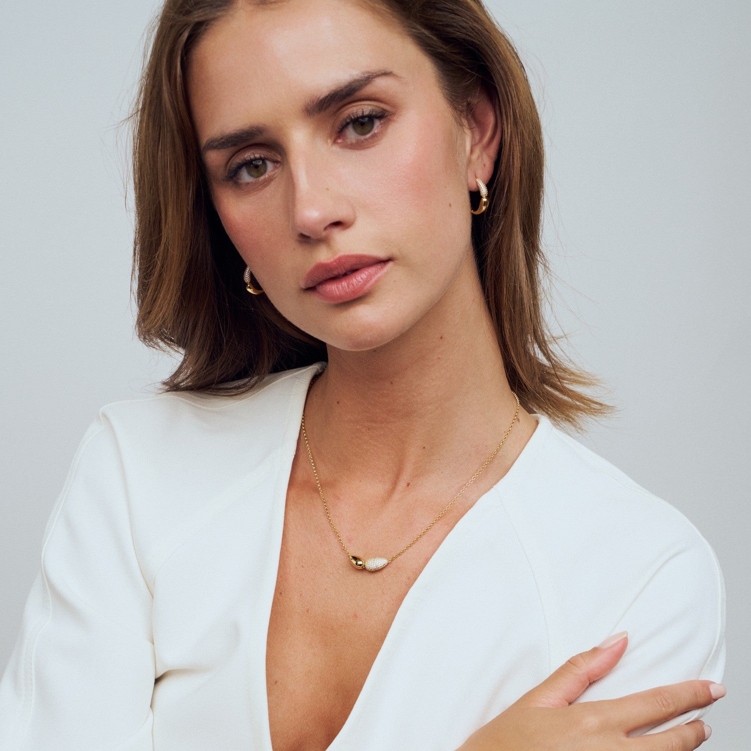 Woman wearing a white top and gold jewelry against a plain background