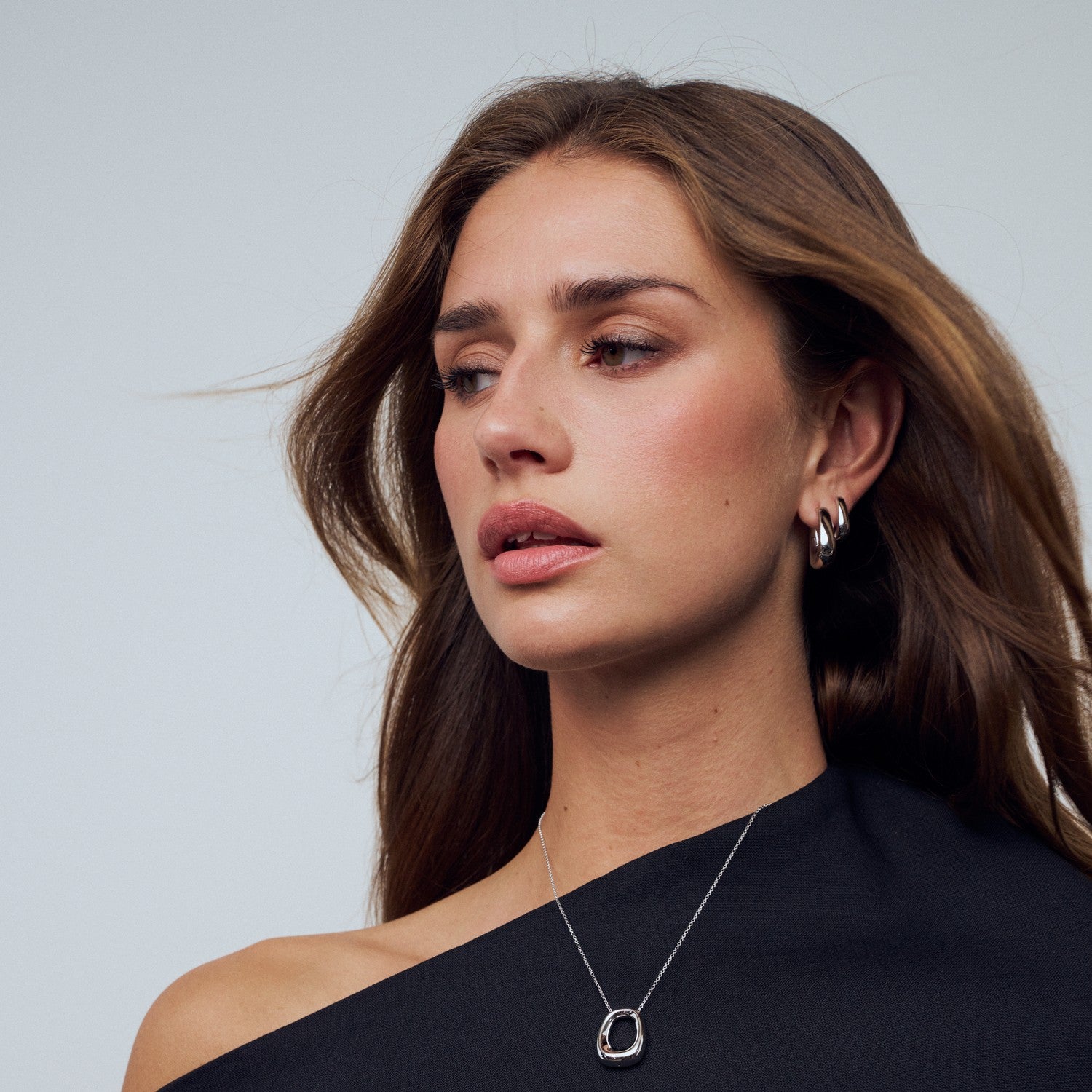 Woman wearing a black top and silver necklace with a plain background