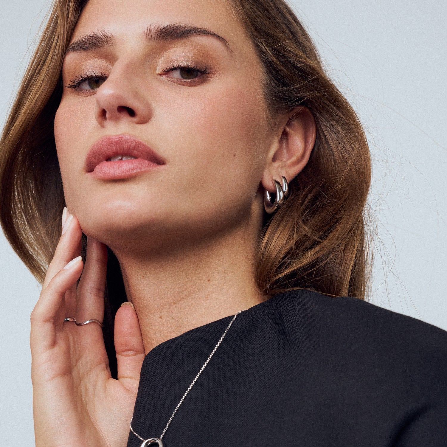 Woman wearing a necklace and earrings against a neutral background