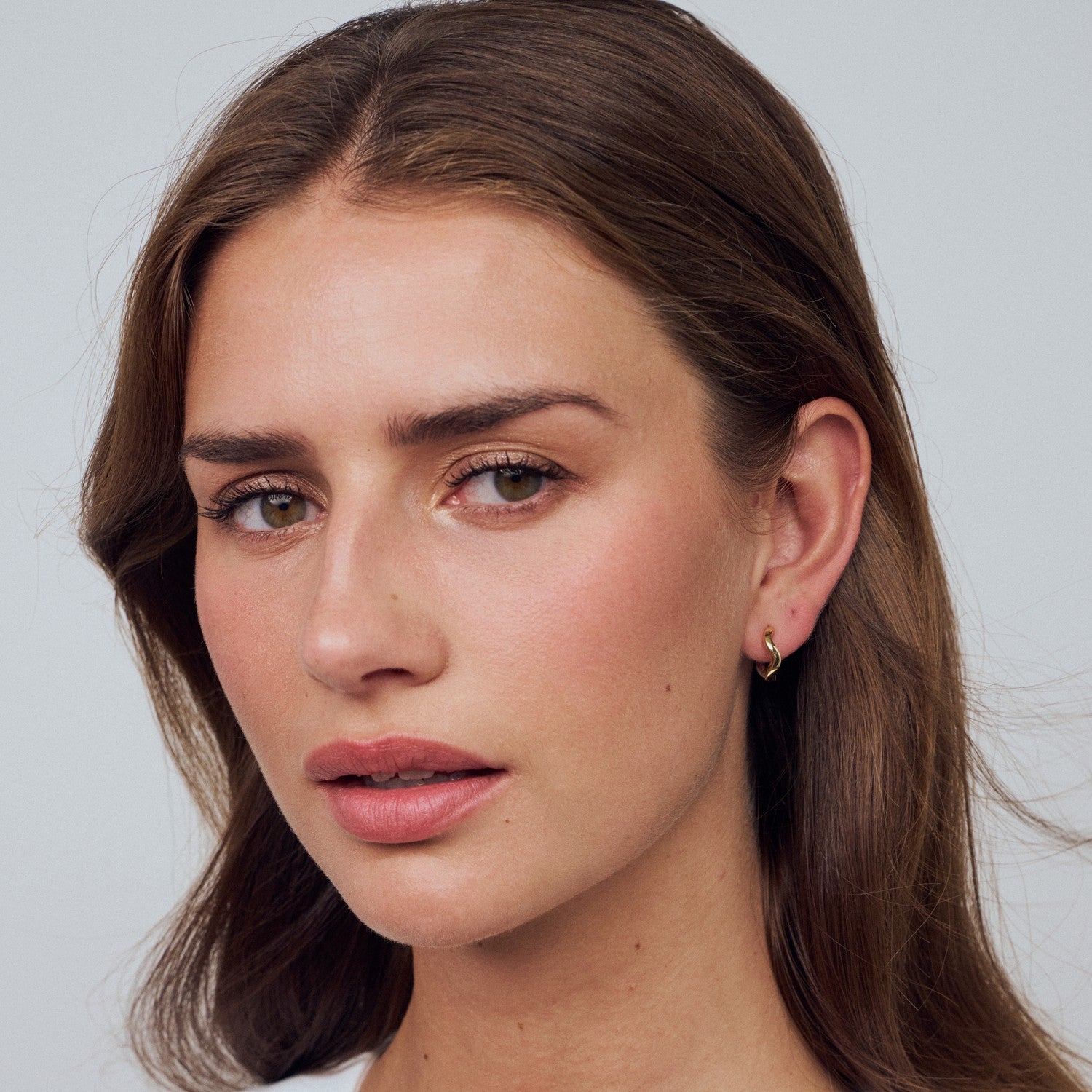 Close-up of a woman with long brown hair and a neutral expression on a light gray background