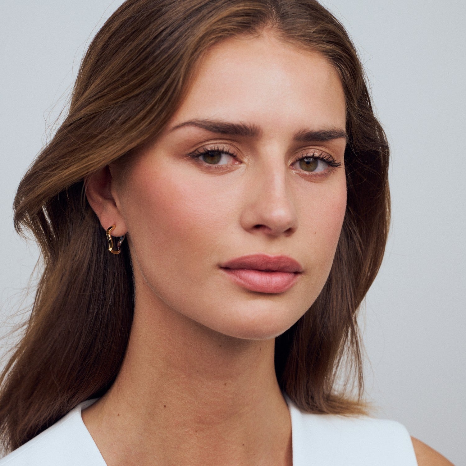 Close-up of a woman with long brown hair and a neutral expression on a light gray background