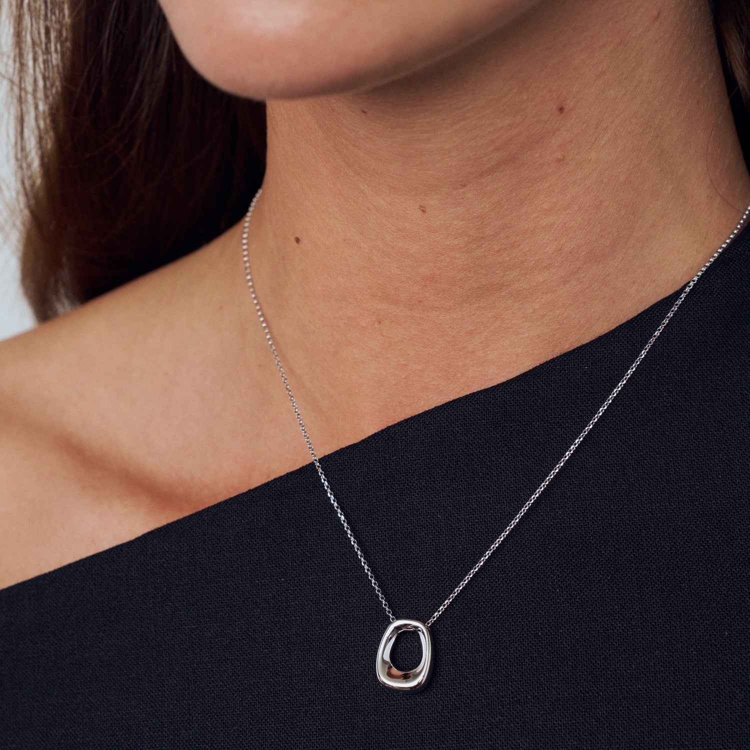 Silver necklace with a unique pendant worn by a person against a neutral background