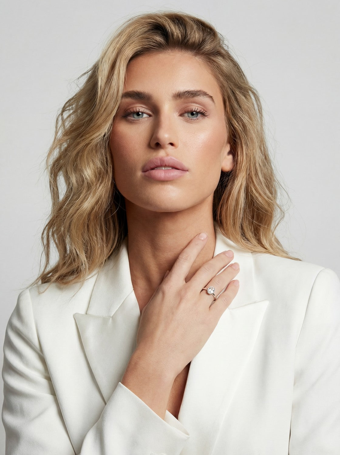 Woman wearing a white blazer with a ring on her finger against a light background
