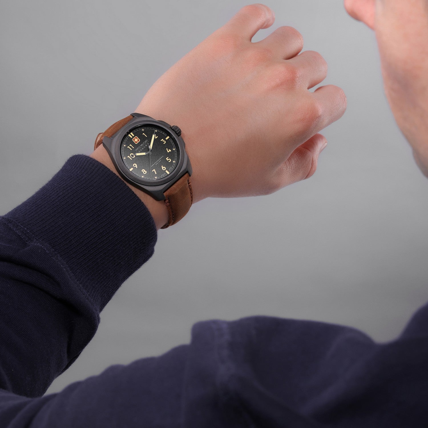 Hand wearing a watch with a brown strap on a gray background